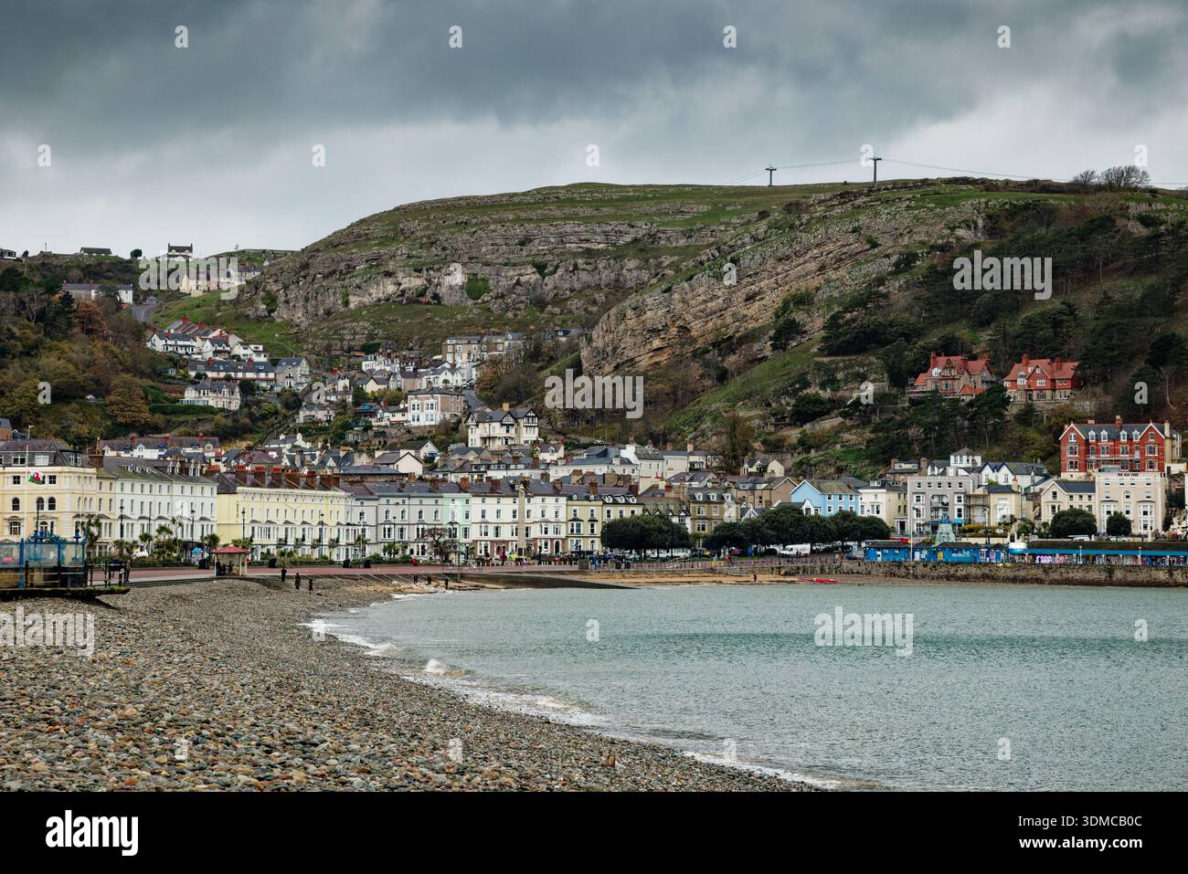 Une journée sereine à la plage avec de douces vagues lançant les galets, le front de mer dominé par d'imposantes falaises calcaires, Llandudno, dans le nord du pays de Galles. Banque D'Images