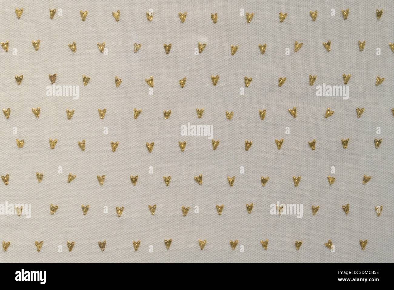 Gros plan détail de tissu blanc avec de petites appliques métalliques en forme d'abeille dorée. Banque D'Images