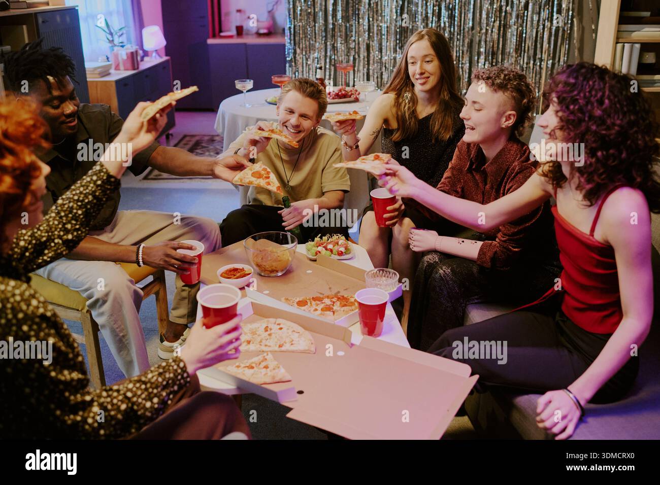 Groupe diversifié de jeunes adultes célébrant et mangeant de la pizza à la fête Banque D'Images