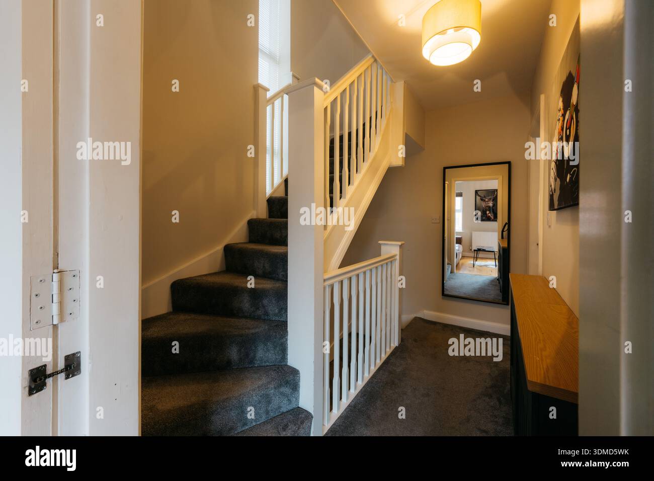 Un couloir avec un escalier et un miroir. L'escalier est en bois et recouvert de tapis. Le couloir est bien éclairé et a une ambiance moderne Banque D'Images