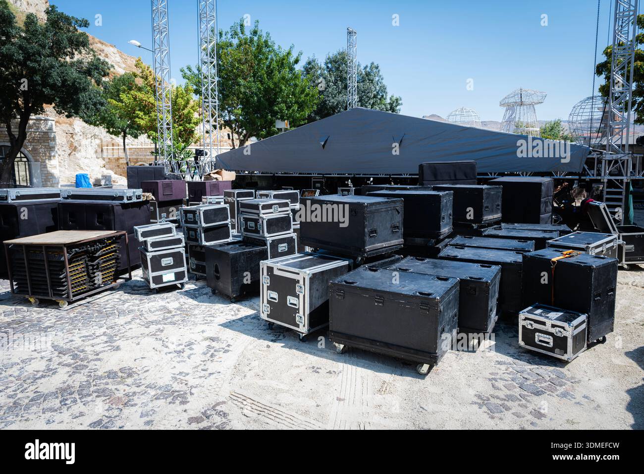 Valises de vol et équipement sonore professionnel sur scène extérieure pavée, préparation de la configuration de concert avec treillis et scène couverte sous ciel clair Banque D'Images