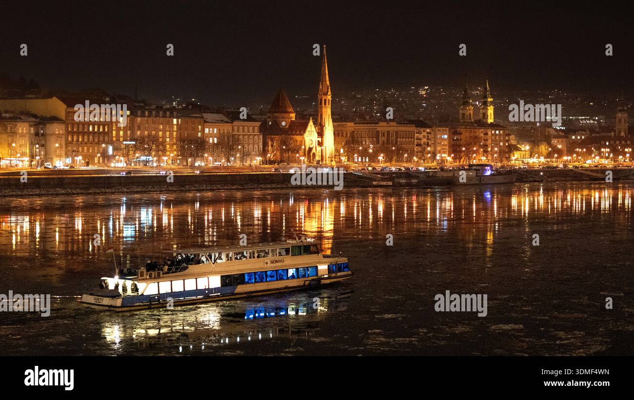 Un bateau de croisière de nuit naviguant sur le Danube avec le front de mer de la ville illuminé et des reflets sur l'eau à Budapest. Banque D'Images
