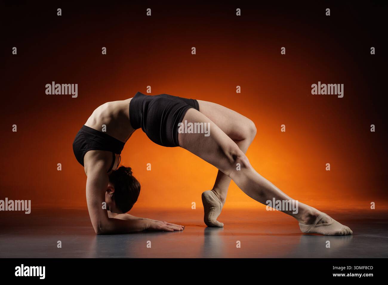 Vue latérale d'une femme flexible faisant l'étirement du dos de l'avant-bras sur le sol du studio avec un fond dégradé orange et un espace de copie pour la bannière du site de fitness o Banque D'Images