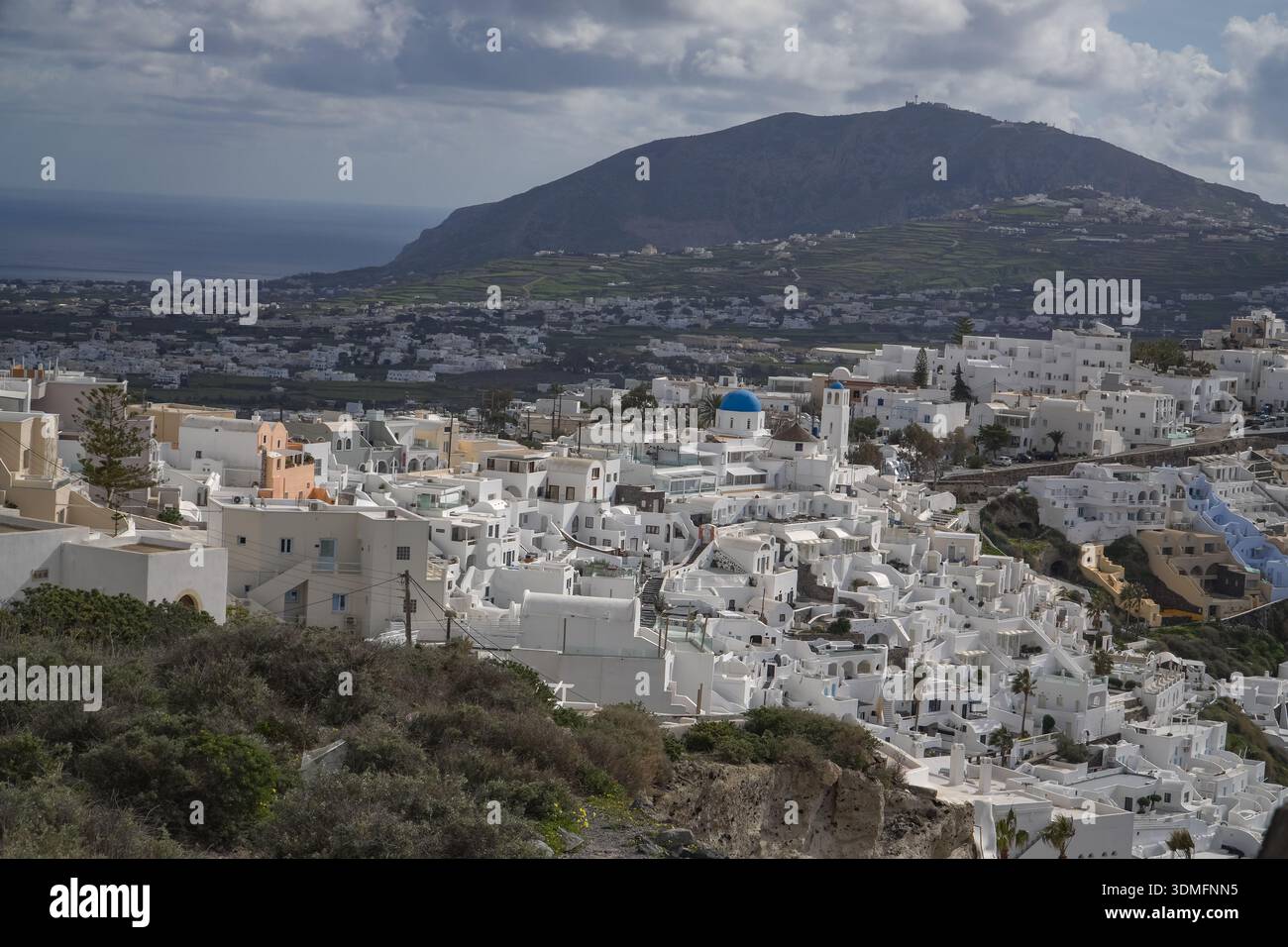 Fira, capitale de Santorin, Grèce. Vue sur les maisons emblématiques des Cyclades blanchies à la chaux regroupées le long du bord de la falaise de la caldeira avec un fond de montagne. Banque D'Images