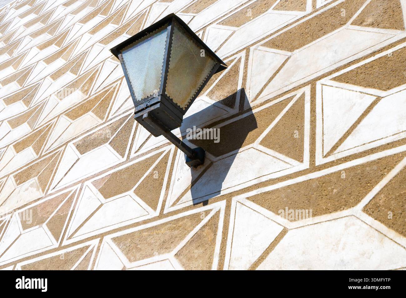 Un lampadaire est fixé à un mur orné de sgraffito plâtre en Trebon. Le design décoratif montre des formes géométriques, créant un visuel intéressant. La lumière du jour améliore les détails. Banque D'Images