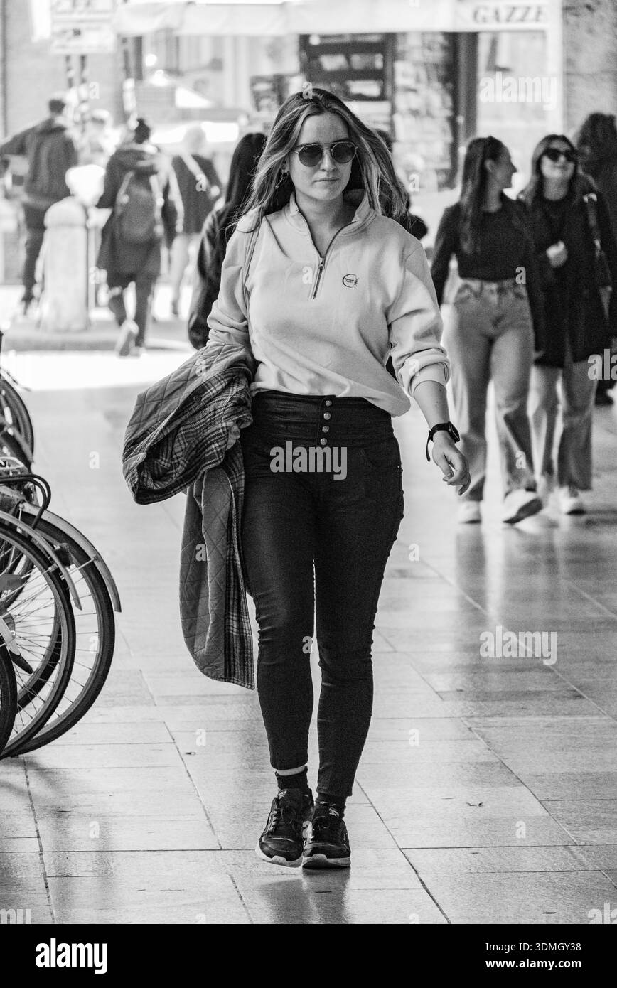 Une jeune femme portant des lunettes de soleil et des vêtements décontractés marche en toute confiance dans une arcade urbaine animée capturée en monochrome à contraste élevé Banque D'Images
