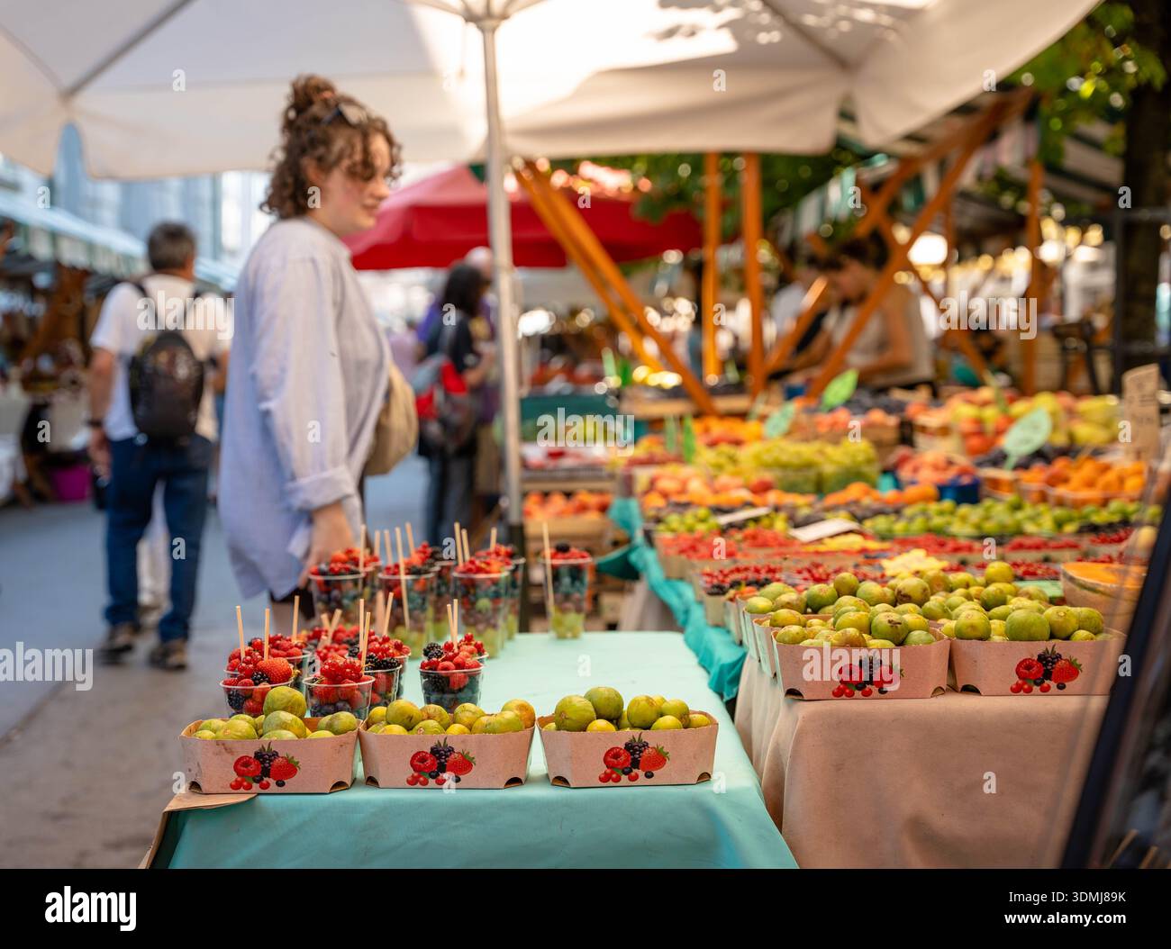 Ljubljana, Slovénie - 10 août 2025 : une jeune femme parcourt un marché en plein air coloré à Ljubljana, où les figues fraîches et les tasses de baies mélangées sont n° Banque D'Images