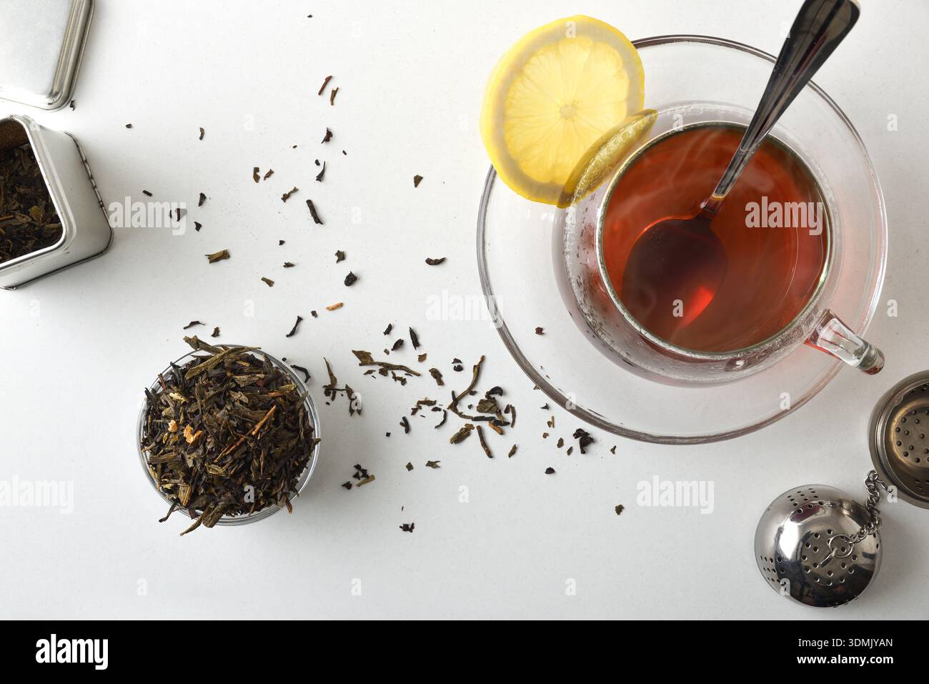 Tasse en verre fraîchement infusée sur une assiette sur un banc de cuisine blanc avec infuseur et récipients pleins d'herbes de thé séchées. Vue de dessus. Banque D'Images