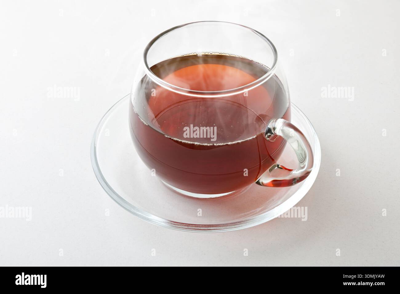 Infusion chaude dans une tasse en verre avec soucoupe isolée sur table blanche. Vue surélevée. Banque D'Images