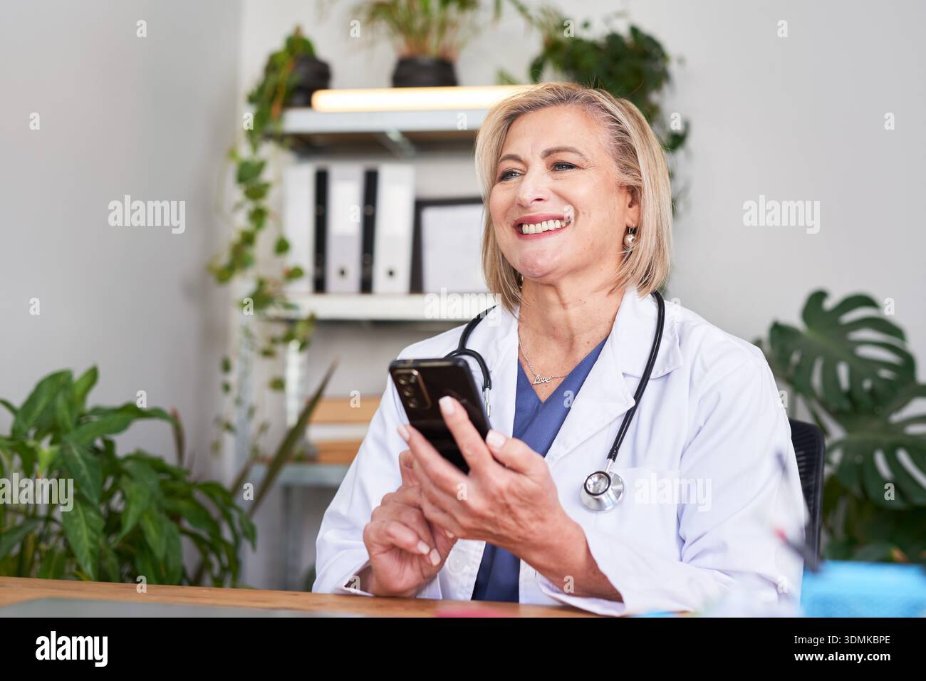 Médecin féminin souriant à l'aide d'un smartphone dans le bureau de clinique avec stéthoscope Banque D'Images