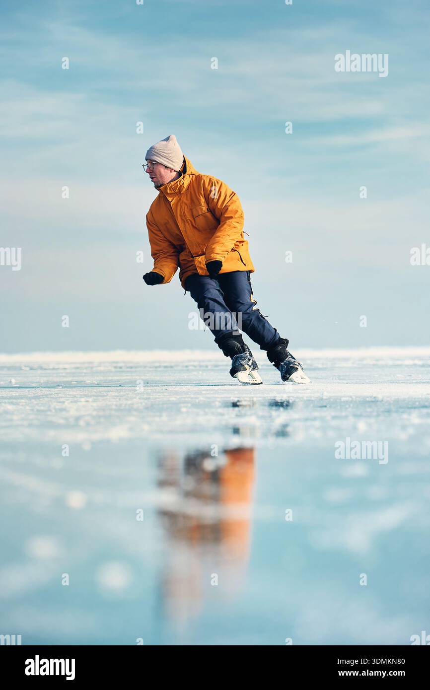 Homme athlète en veste jaune patin sur glace sur le lac gelé avec des fissures et de la neige à l'heure d'hiver Banque D'Images