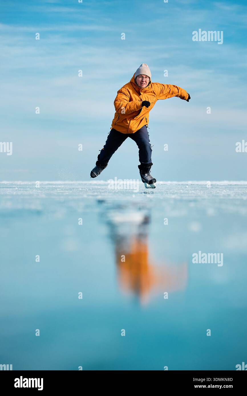 Homme athlète en veste jaune patin sur glace sur le lac gelé avec des fissures et de la neige à l'heure d'hiver Banque D'Images