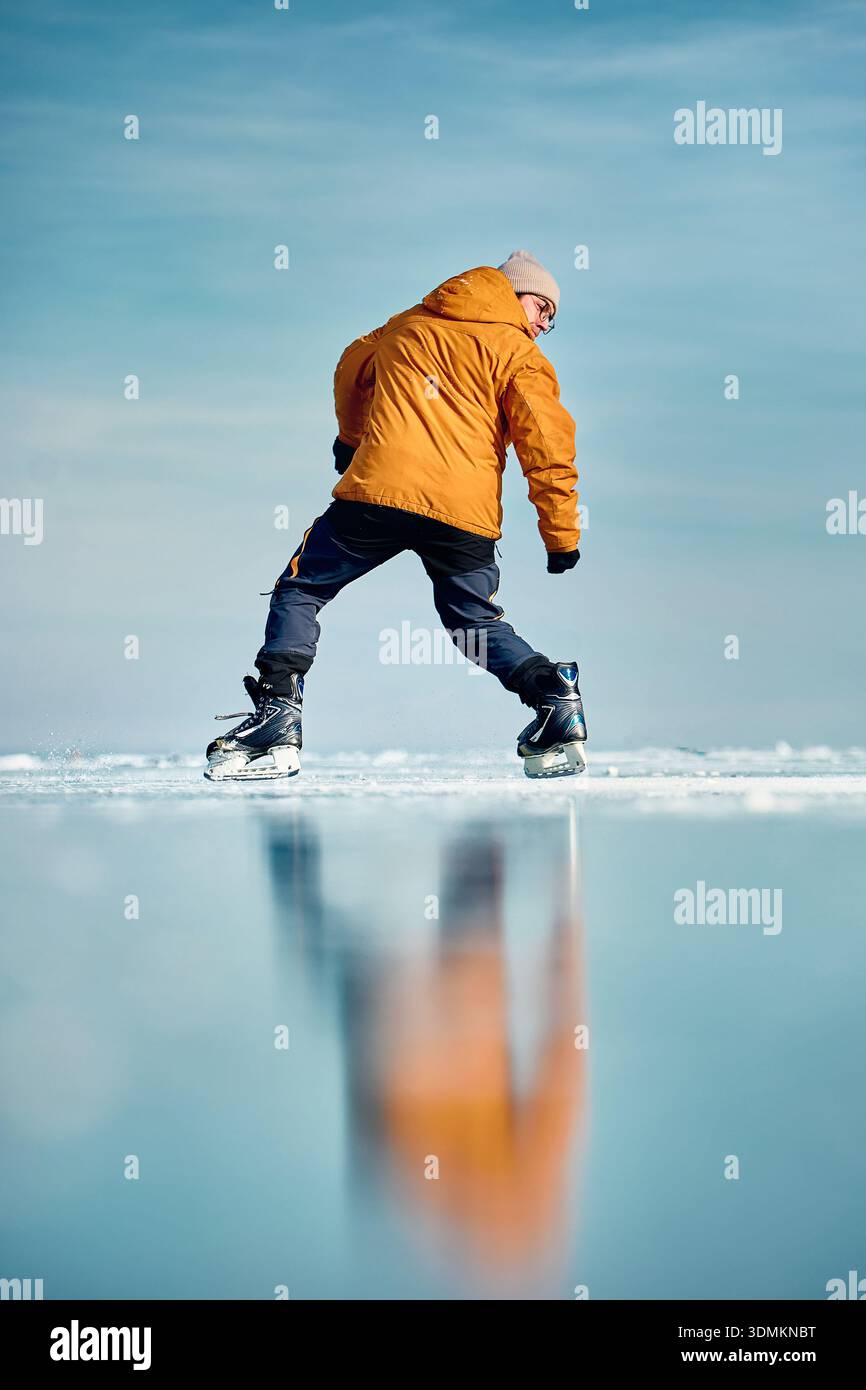 Homme athlète en veste jaune patin sur glace sur le lac gelé avec des fissures et de la neige à l'heure d'hiver Banque D'Images