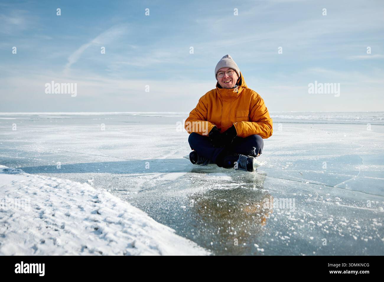 Portrait de l'athlète homme en veste jaune patineuse sur glace sur lac gelé avec des fissures et de la neige à l'heure d'hiver Banque D'Images