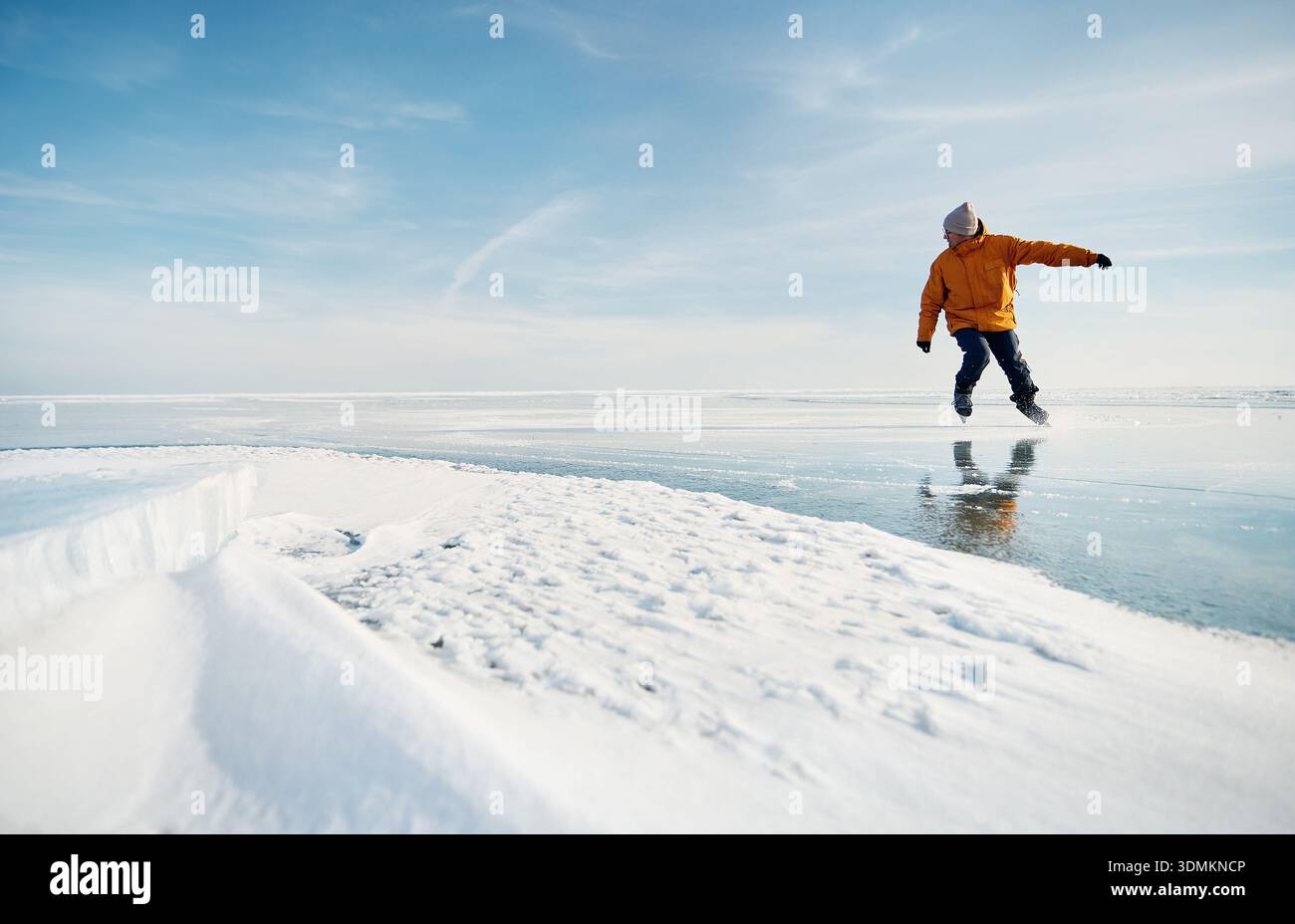 Homme athlète en veste jaune patin sur glace sur le lac gelé avec des fissures et de la neige à l'heure d'hiver Banque D'Images