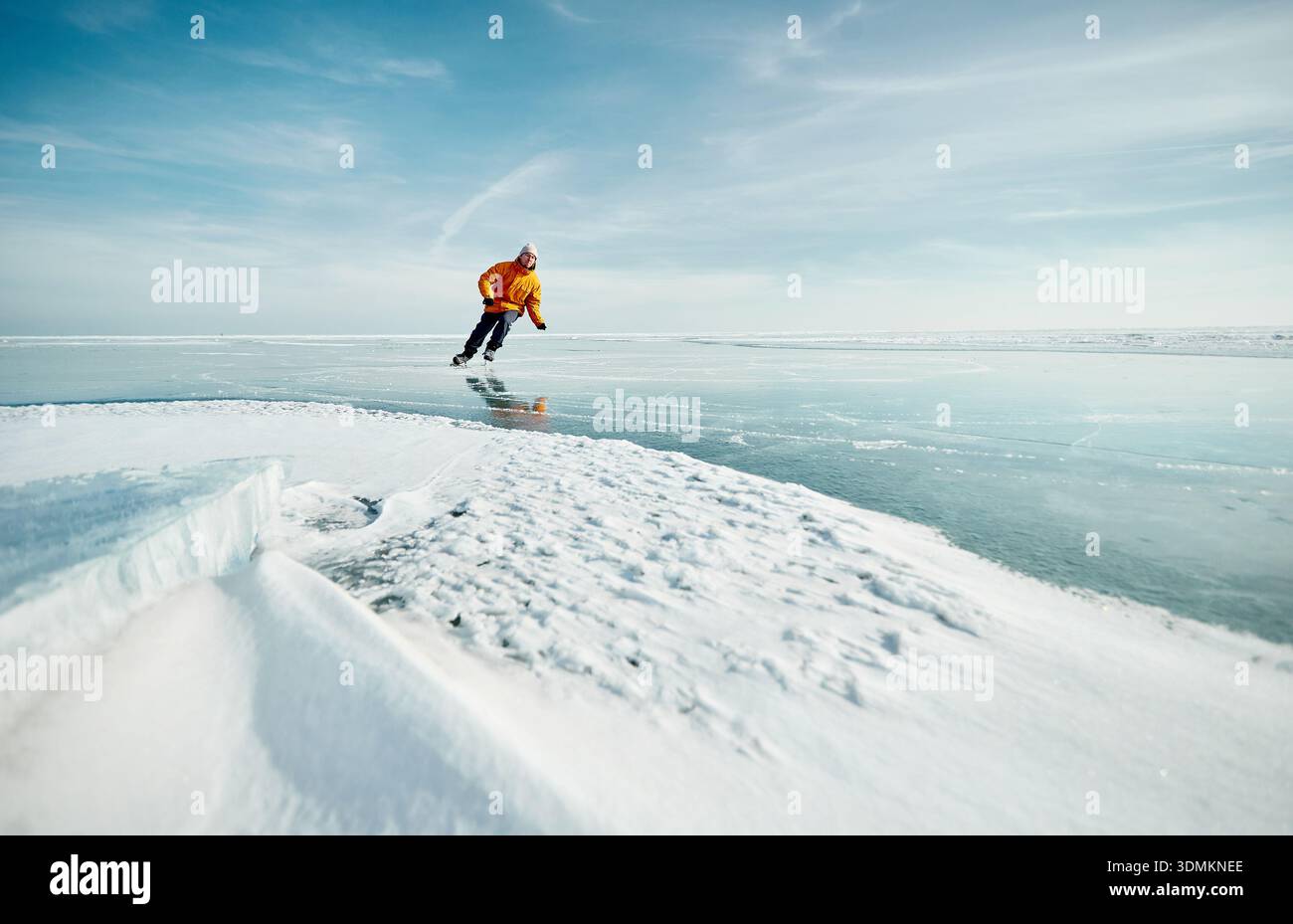 Homme athlète en veste jaune patin sur glace sur le lac gelé avec des fissures et de la neige à l'heure d'hiver Banque D'Images