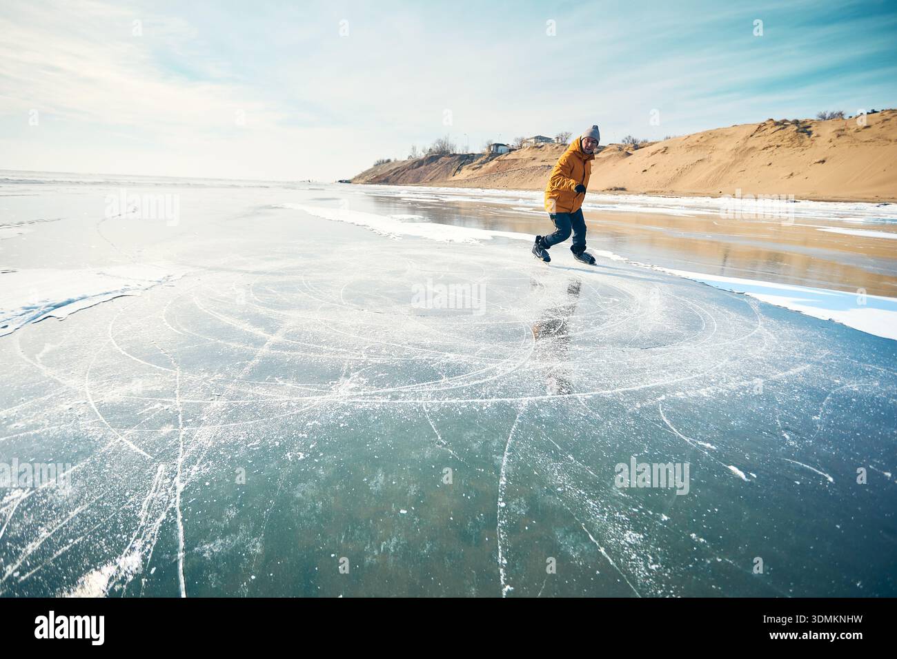 Homme athlète en veste jaune patin sur glace sur le lac gelé avec des fissures et de la neige à l'heure d'hiver Banque D'Images