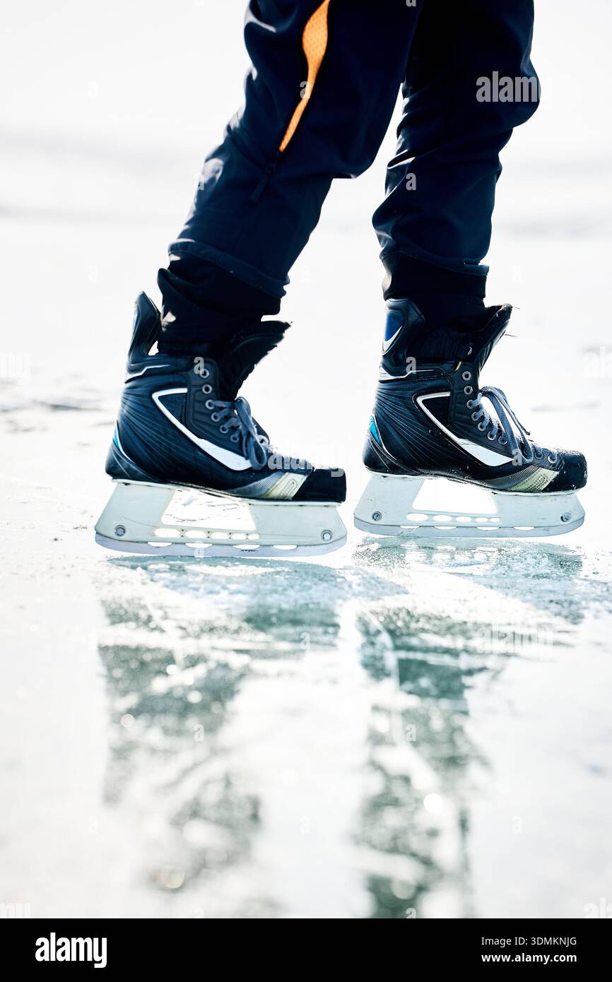 Homme athlète patin sur glace sur le lac gelé avec des fissures et de la neige en hiver. Gros plan de jambe de patin à glace Banque D'Images