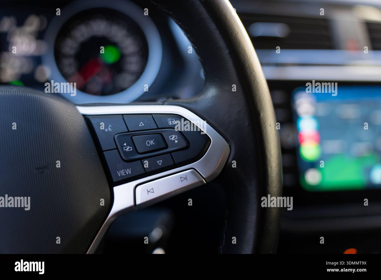 Cockpit de voiture moderne gros plan avec commandes multimédia au volant, bouton OK et touches directionnelles, cadran d'instrument et écran tactile en douceur hors de f Banque D'Images