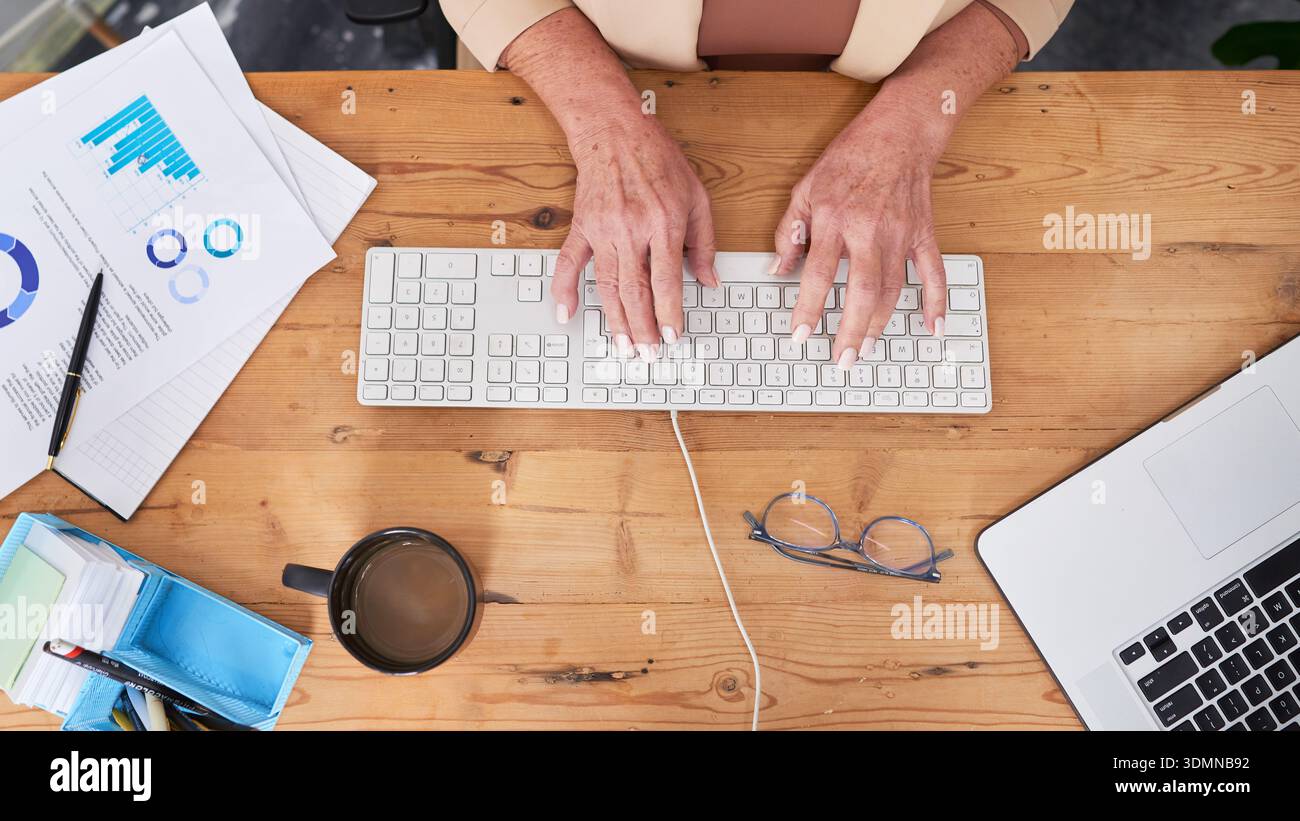 Professionnel des affaires travaillant au bureau en bois avec clavier, ordinateur portable, café, documents, graphiques, et lunettes Banque D'Images