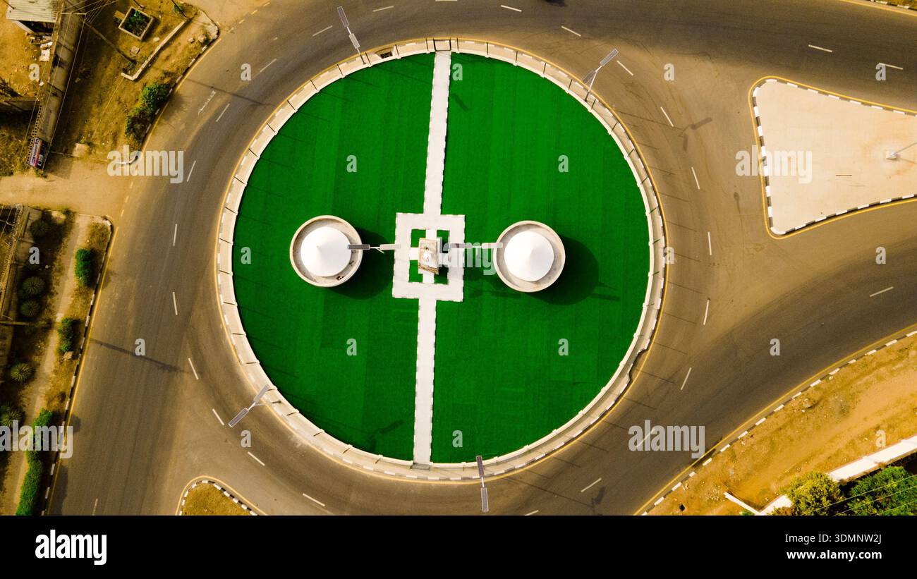 Vue aérienne d'un rond-point vert vibrant avec des caractéristiques architecturales blanches se détache contre les routes asphaltées sombres, Ilorin, Kwara, Nigeria. Banque D'Images