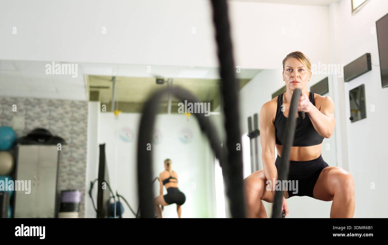 Femme déterminée s'entrainant avec des cordes de combat dans le gymnase Banque D'Images