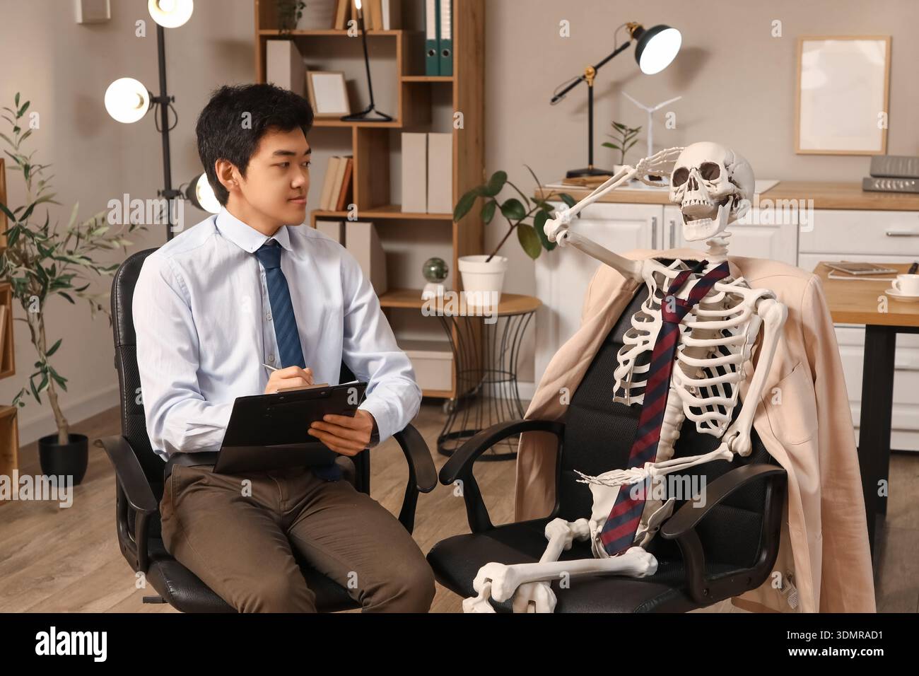 Jeune homme d'affaires asiatique avec squelette humain travaillant dans le bureau Banque D'Images