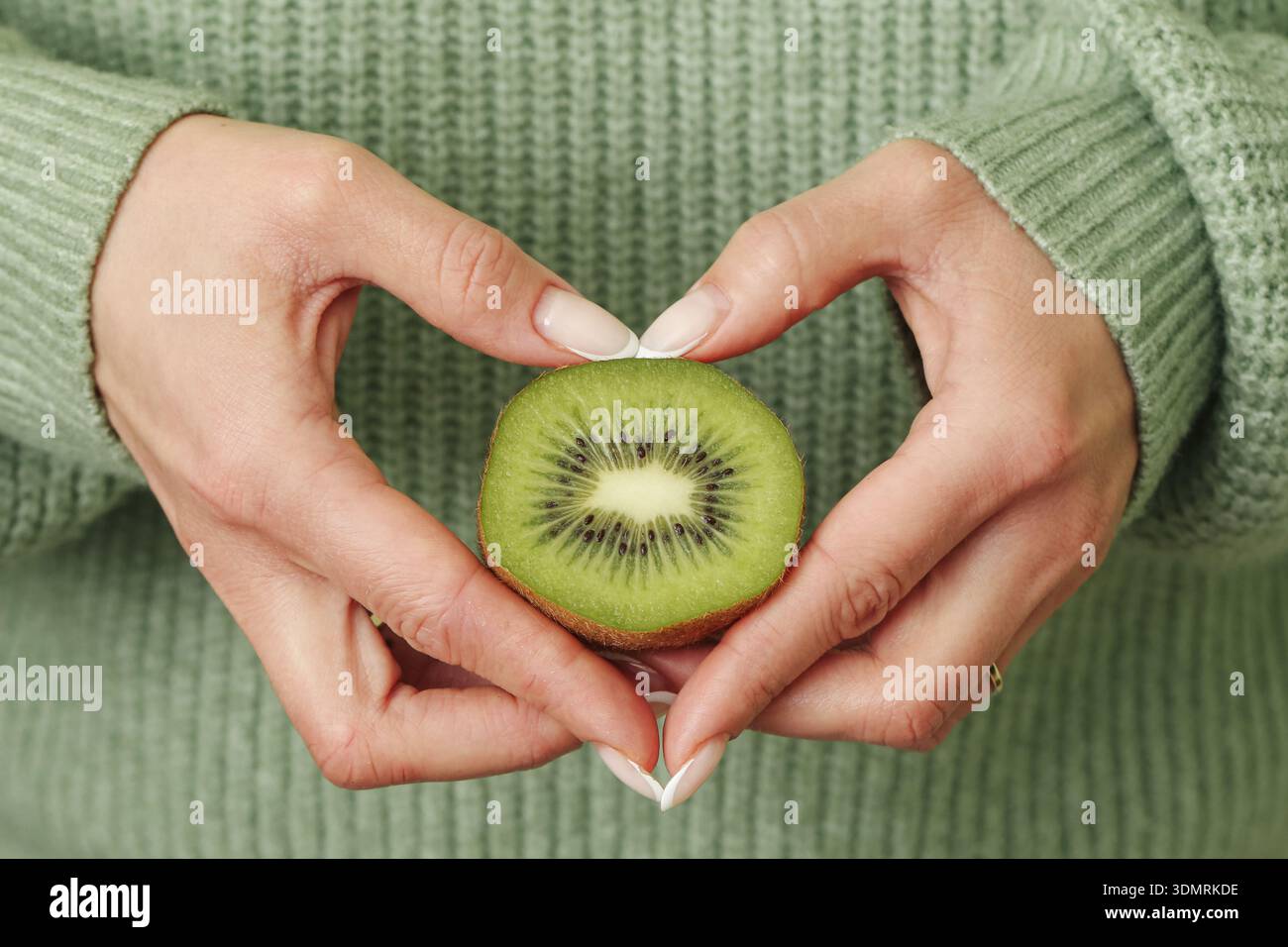 Femme tenant des kiwis dans un geste de mains en forme de coeur. Nutrition saine et concept de vitamine naturelle avec des aliments tropicaux frais à l'intérieur. Banque D'Images