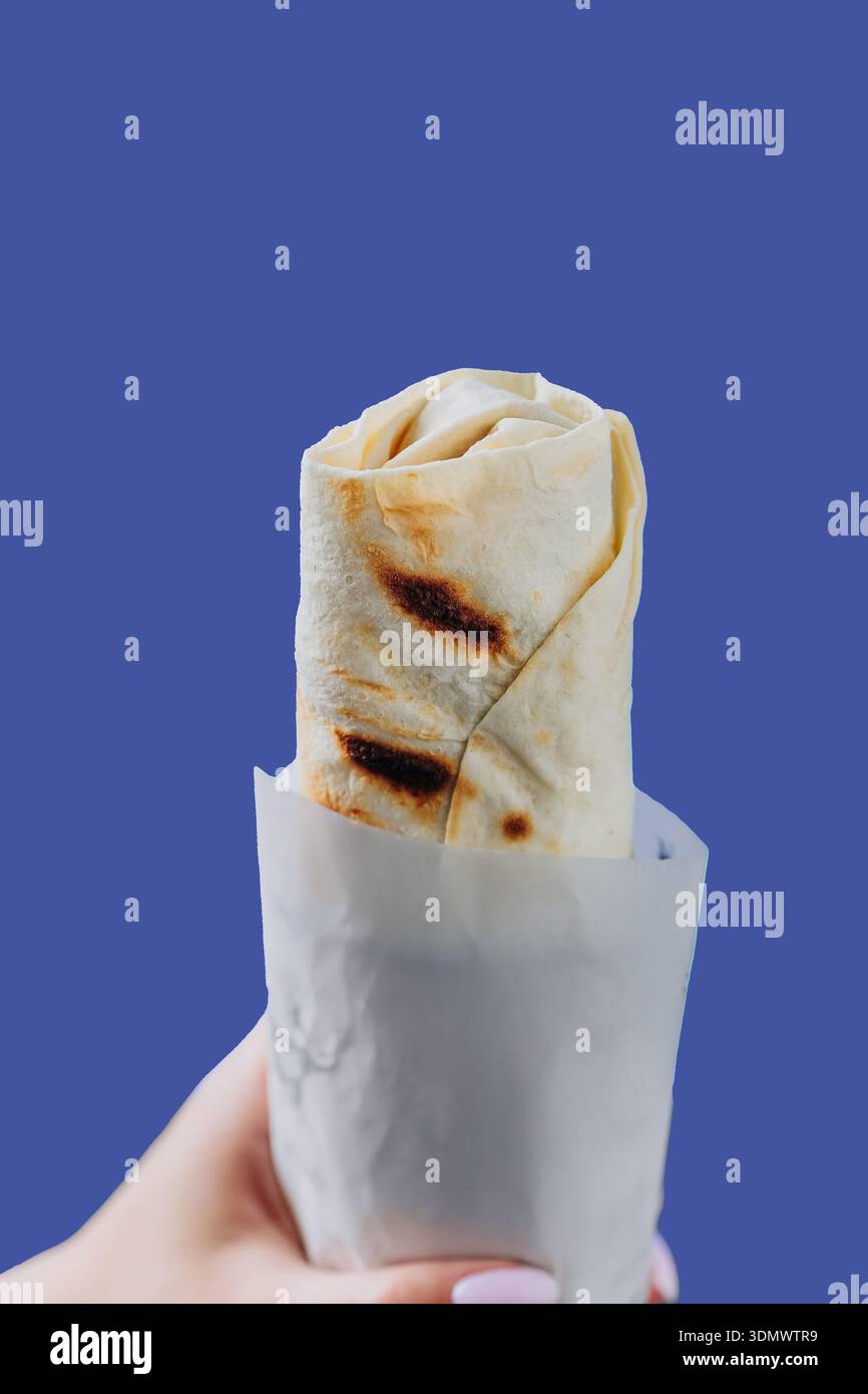 Main tenant shawarma enveloppé dans une pochette en papier isolé sur fond bleu Banque D'Images