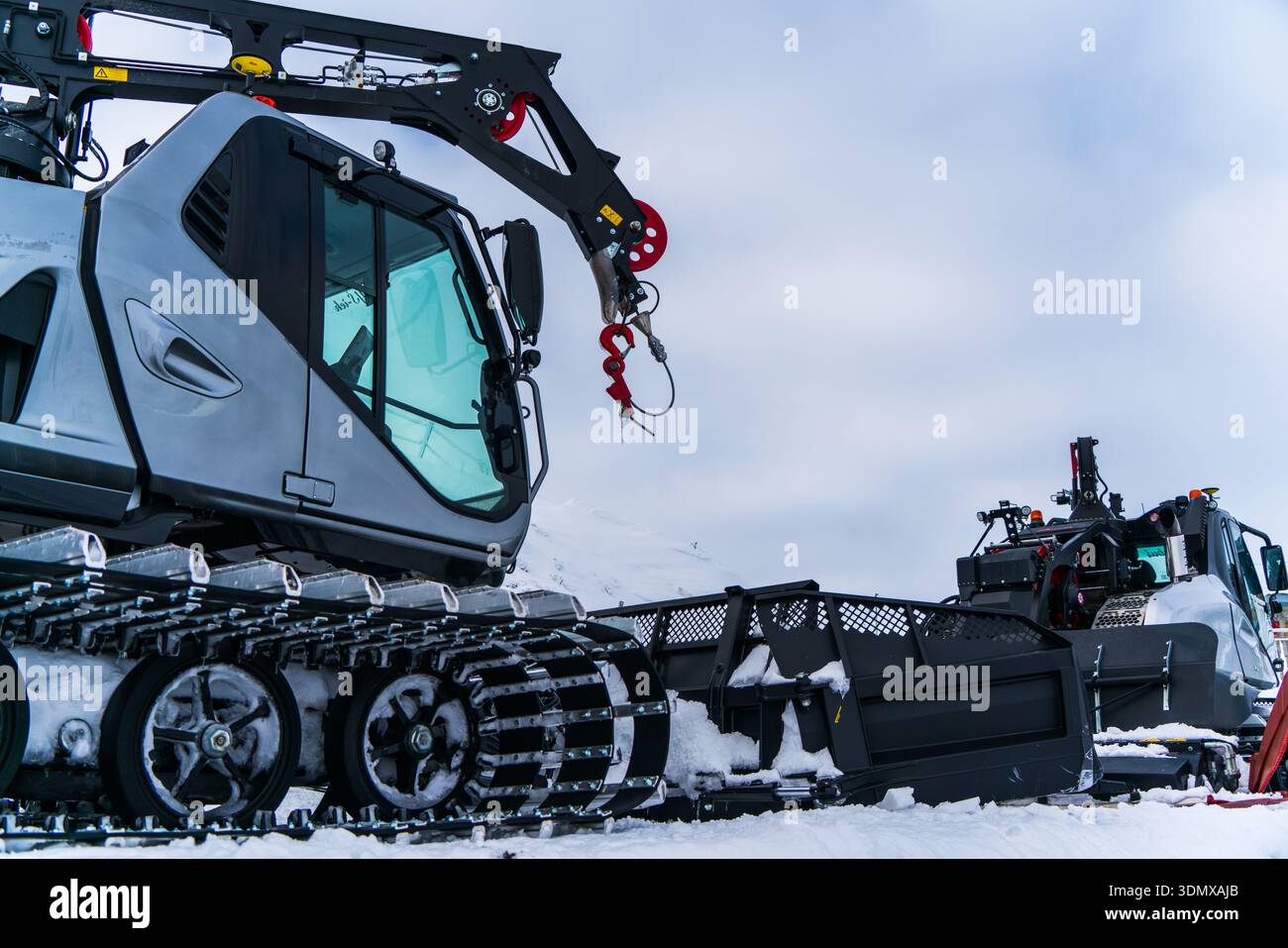 Deux machines de toilettage de neige positionnées sur une pente de montagne enneigée, avec grues et trains d'atterrissage à chenilles visibles, représentant une station de ski professionnelle Banque D'Images