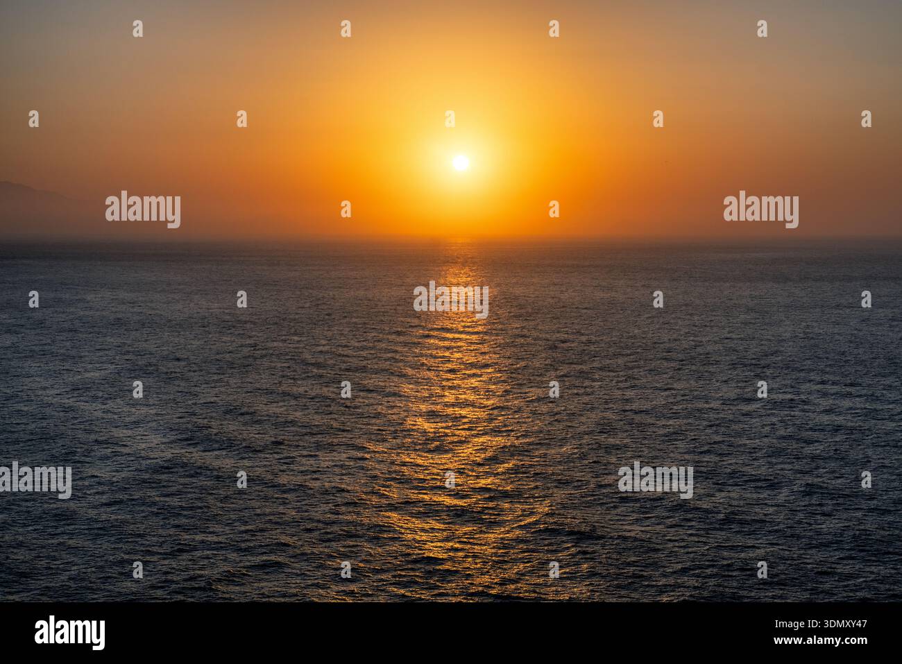 Coucher de soleil doré paisible sur la mer Méditerranée avec un ciel orange chaud et un reflet chatoyant sur la surface de l'eau calme, créant un calme et minima Banque D'Images