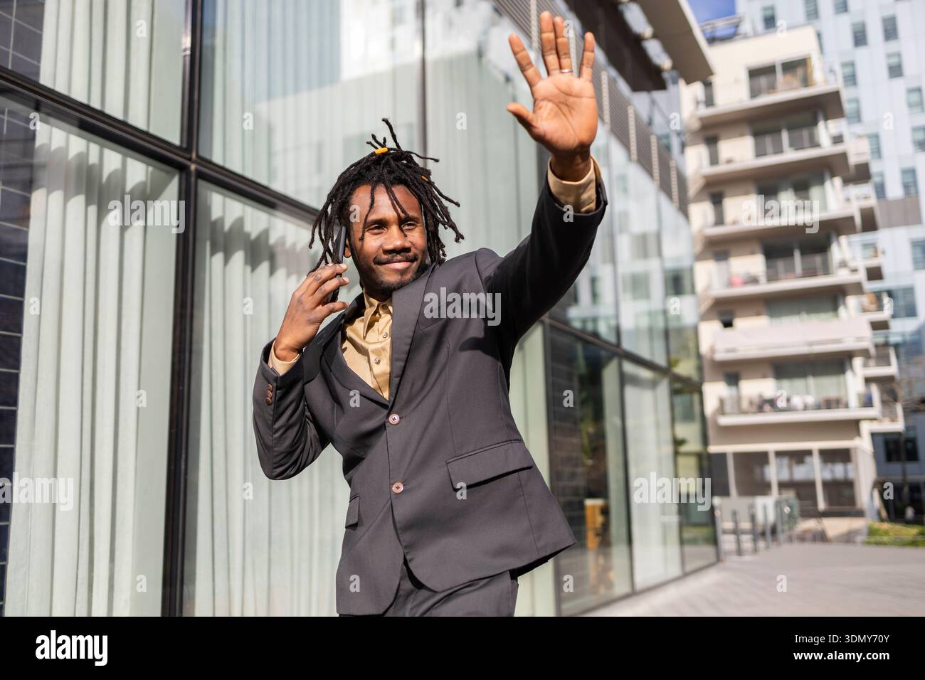 Homme d'affaires afro-américain avec des dreadlocks posant en toute confiance à l'extérieur dans un cadre urbain. Il porte un costume noir élégant, exsudant un sens de p Banque D'Images