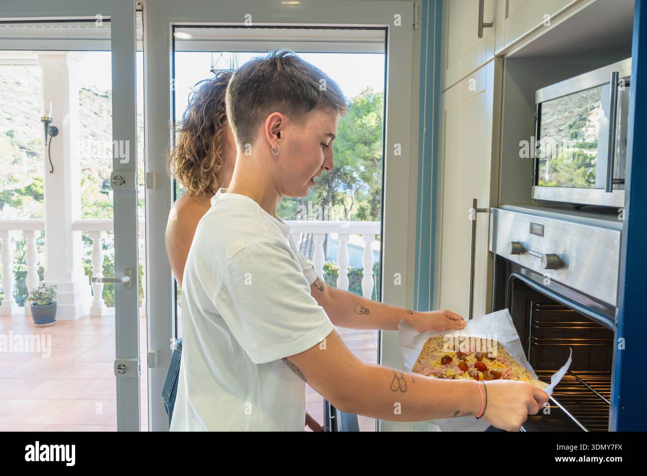 Deux amis souriants alors qu'ils préparent un délicieux repas fait maison dans une cuisine ensoleillée, partageant des moments joyeux et des compétences culinaires tout en faisant cuire une eau de bouche Banque D'Images