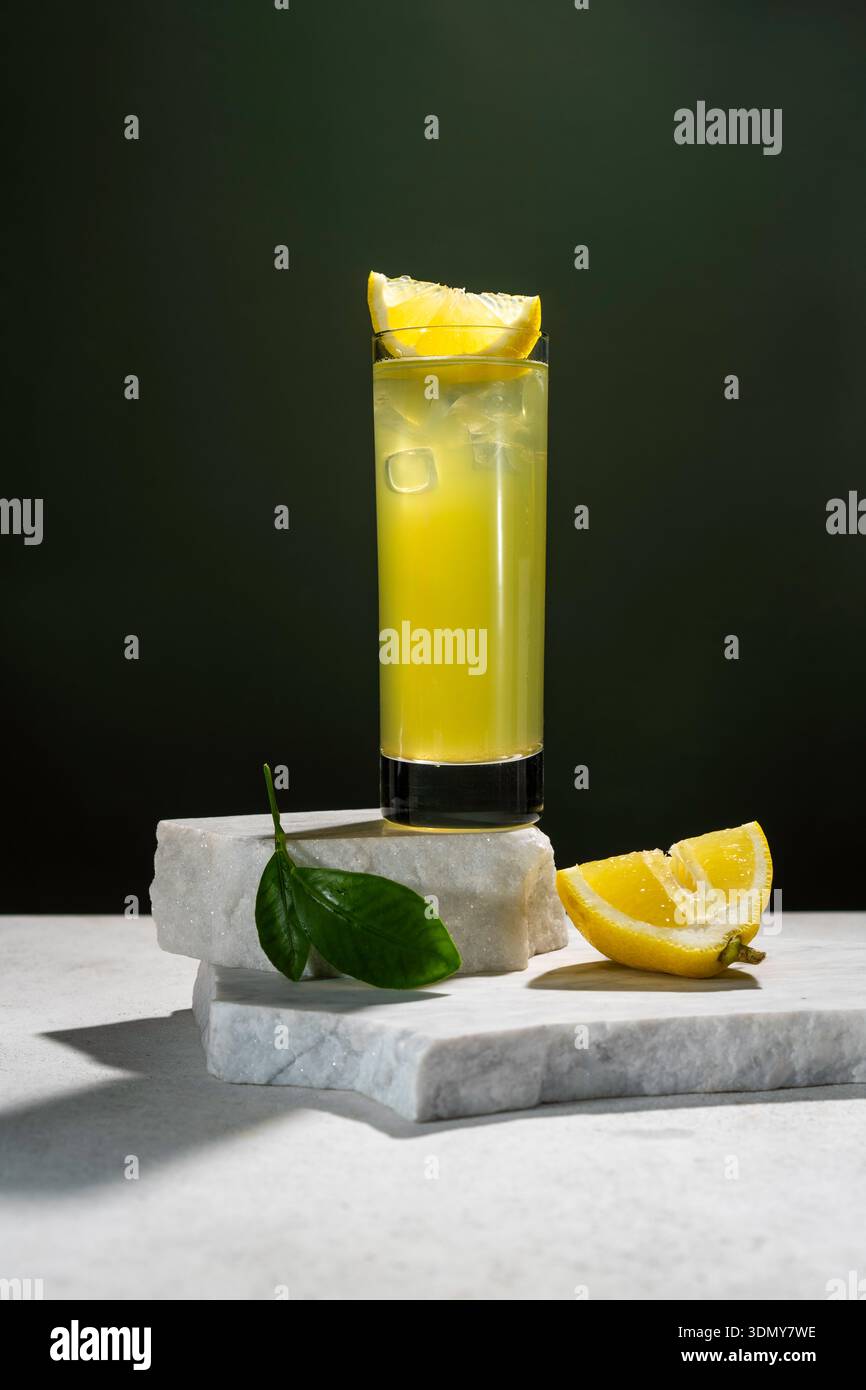 Un grand verre de thé glacé au citron frais est placé sur un fond sombre, garni d'un coin de citron. La boisson repose sur des dalles de marbre, avec du citron frais Banque D'Images