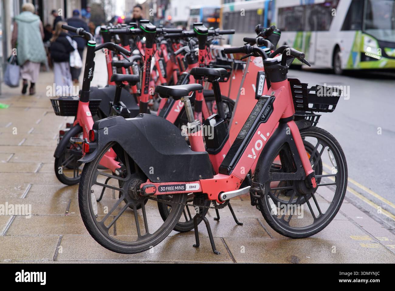 Rangée de scooters électriques VOI rouges garés sur un trottoir du centre-ville de Cambridge près d'un bus. Cambridge, Angleterre Banque D'Images