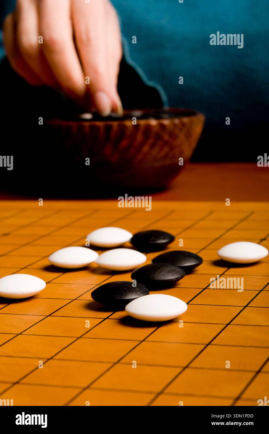 Gros plan d'une main plaçant des pierres sur un plateau de Go, symbolisant la pensée stratégique, la patience et le jeu de plateau abstrait classique Banque D'Images