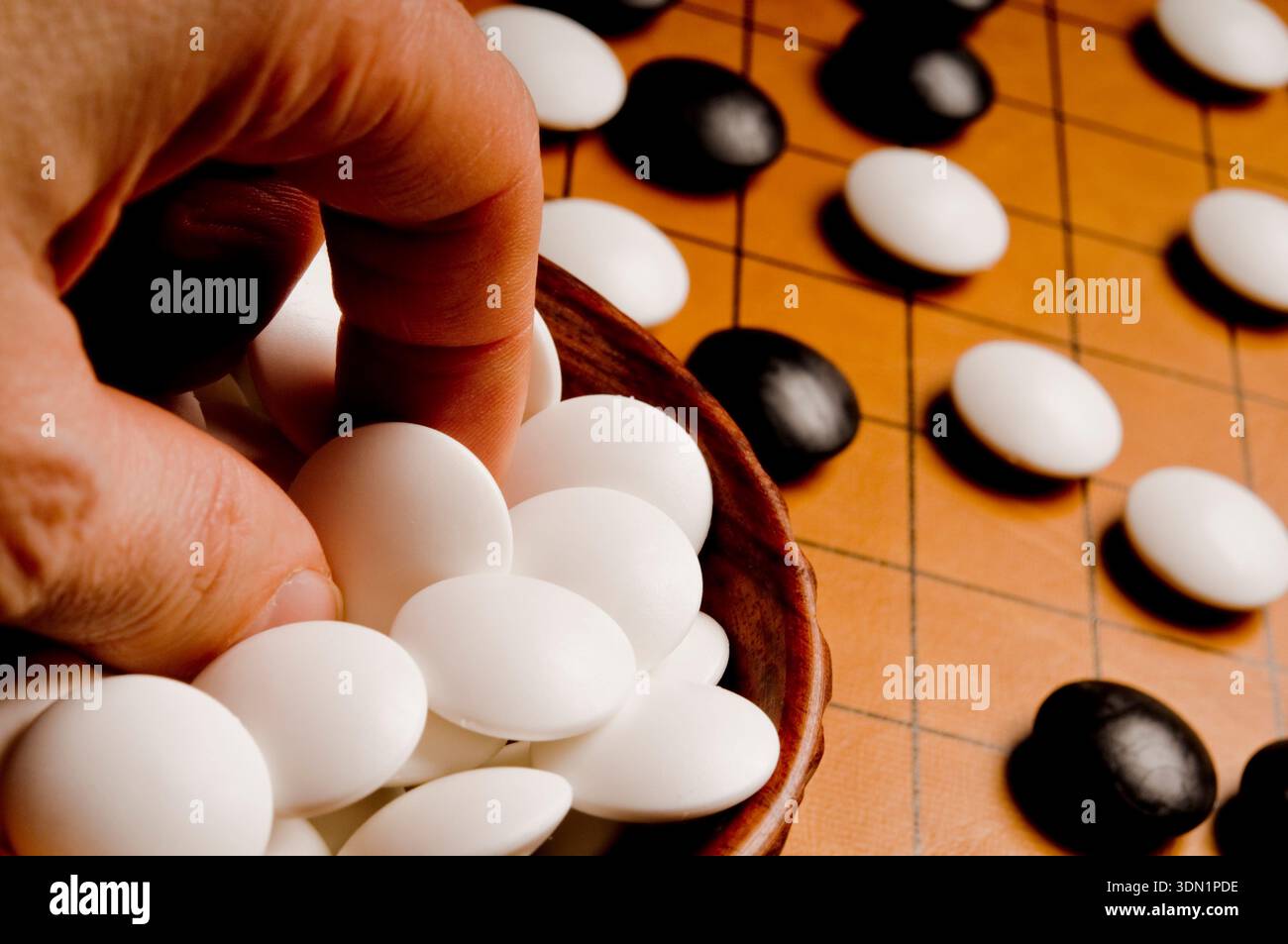 Gros plan d'une main plaçant des pierres sur un plateau de Go, symbolisant la pensée stratégique, la patience et le jeu de plateau abstrait classique Banque D'Images