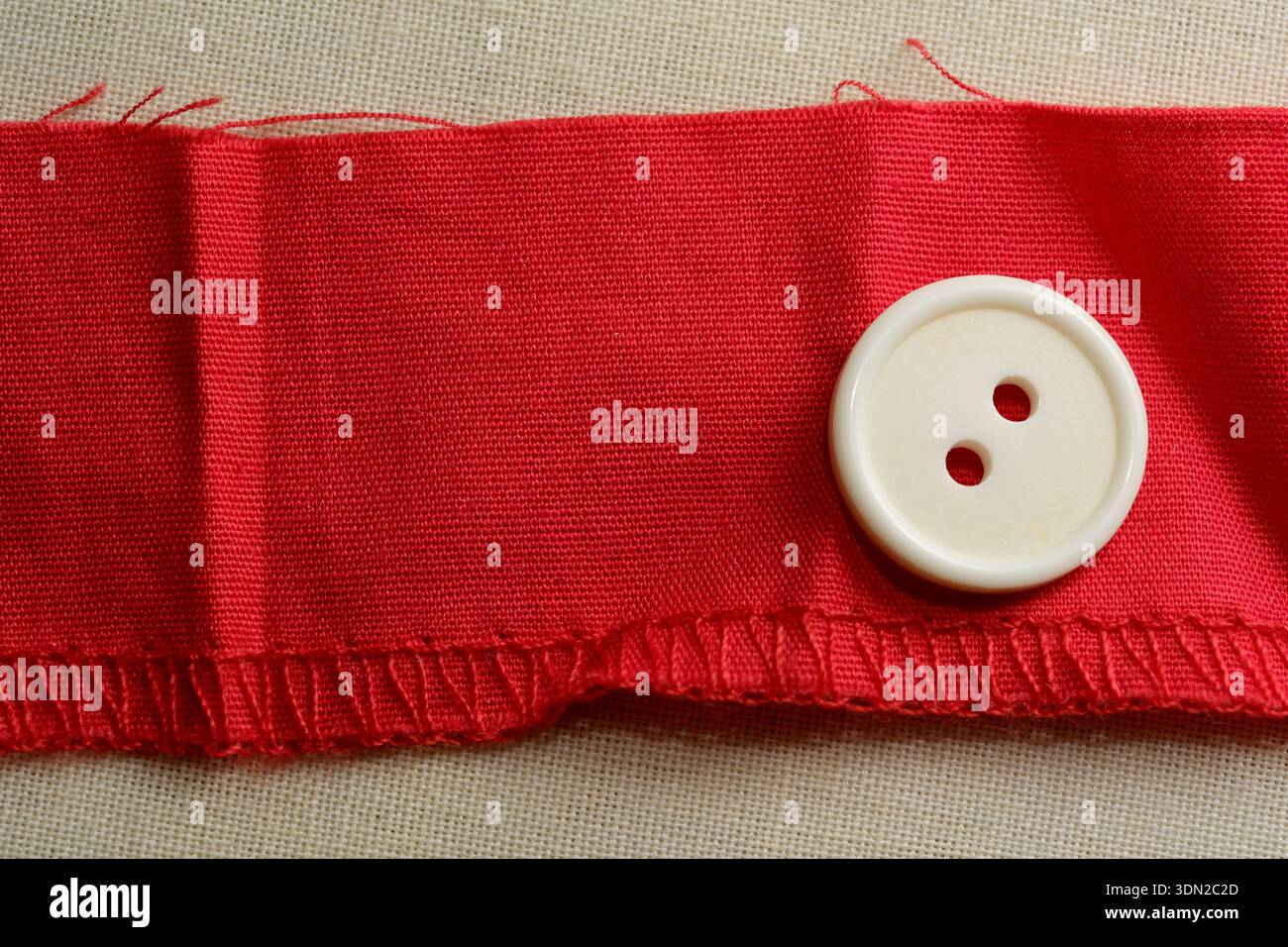 Un ruban en tissu rouge saisissant se pose à plat avec un bouton blanc classique posé sur le dessus. Banque D'Images