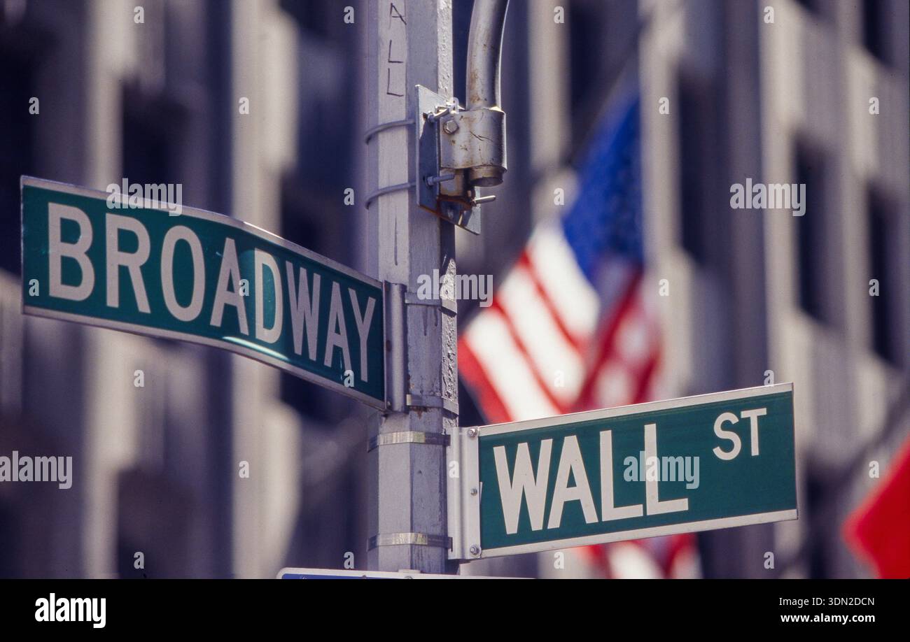 USA, New York City, panneaux de rue de Broadway et Wall Street devant un drapeau américain. Banque D'Images