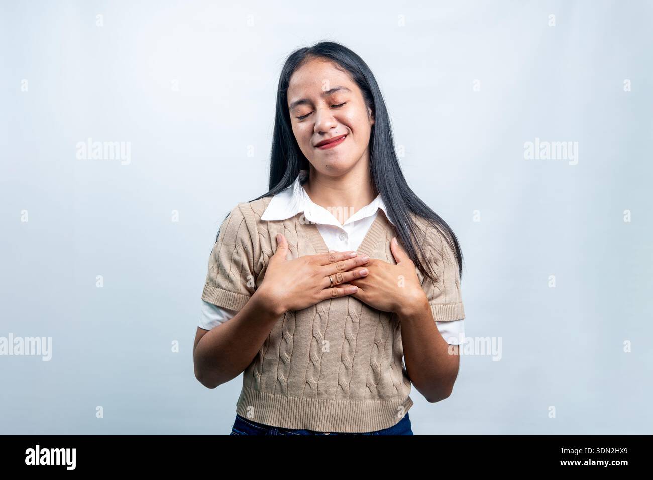 Une jeune femme asiatique les yeux fermés et les mains sur la poitrine, exprimant gratitude, paix et sincérité, isolée sur un fond blanc propre. Banque D'Images