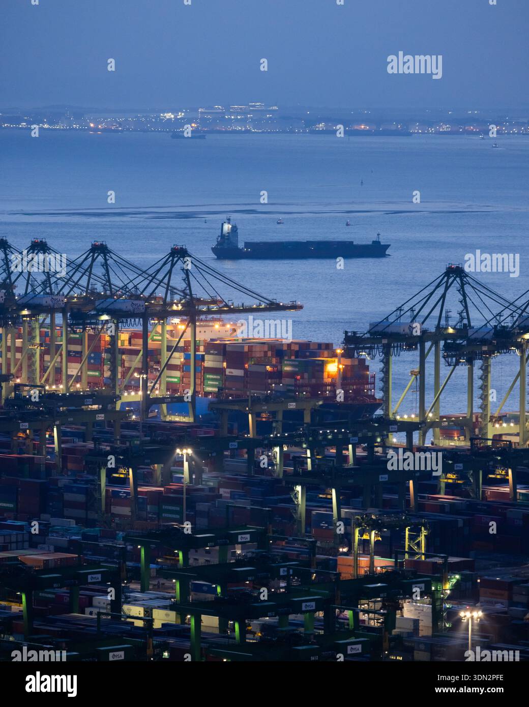 Vue sur le port de Singapour au crépuscule nocturne avec des cargos et des conteneurs et des grues au terminal de Pasir Panjang Banque D'Images