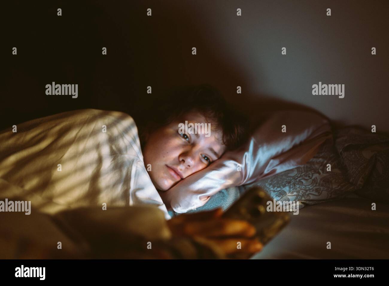 la jeune femme utilise un smartphone la nuit lorsqu'elle est allongée dans son lit Banque D'Images