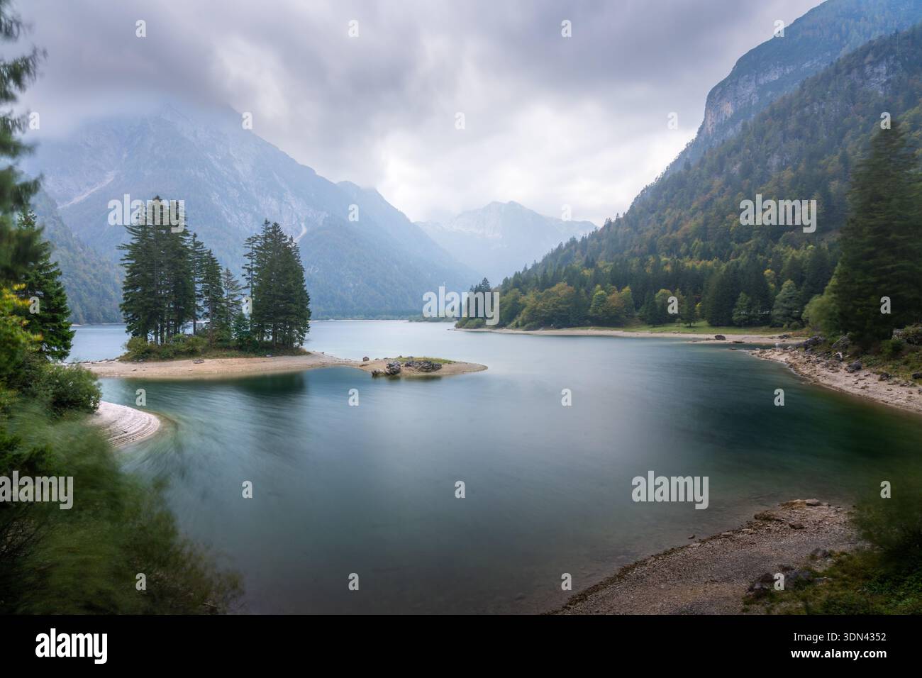 Vue aérienne des eaux tranquilles reflétant le ciel couvant, encadrée par l'étreinte accidentée des Alpes juliennes et des forêts luxuriantes, du Trentin, du Frioul-Vénétie Banque D'Images