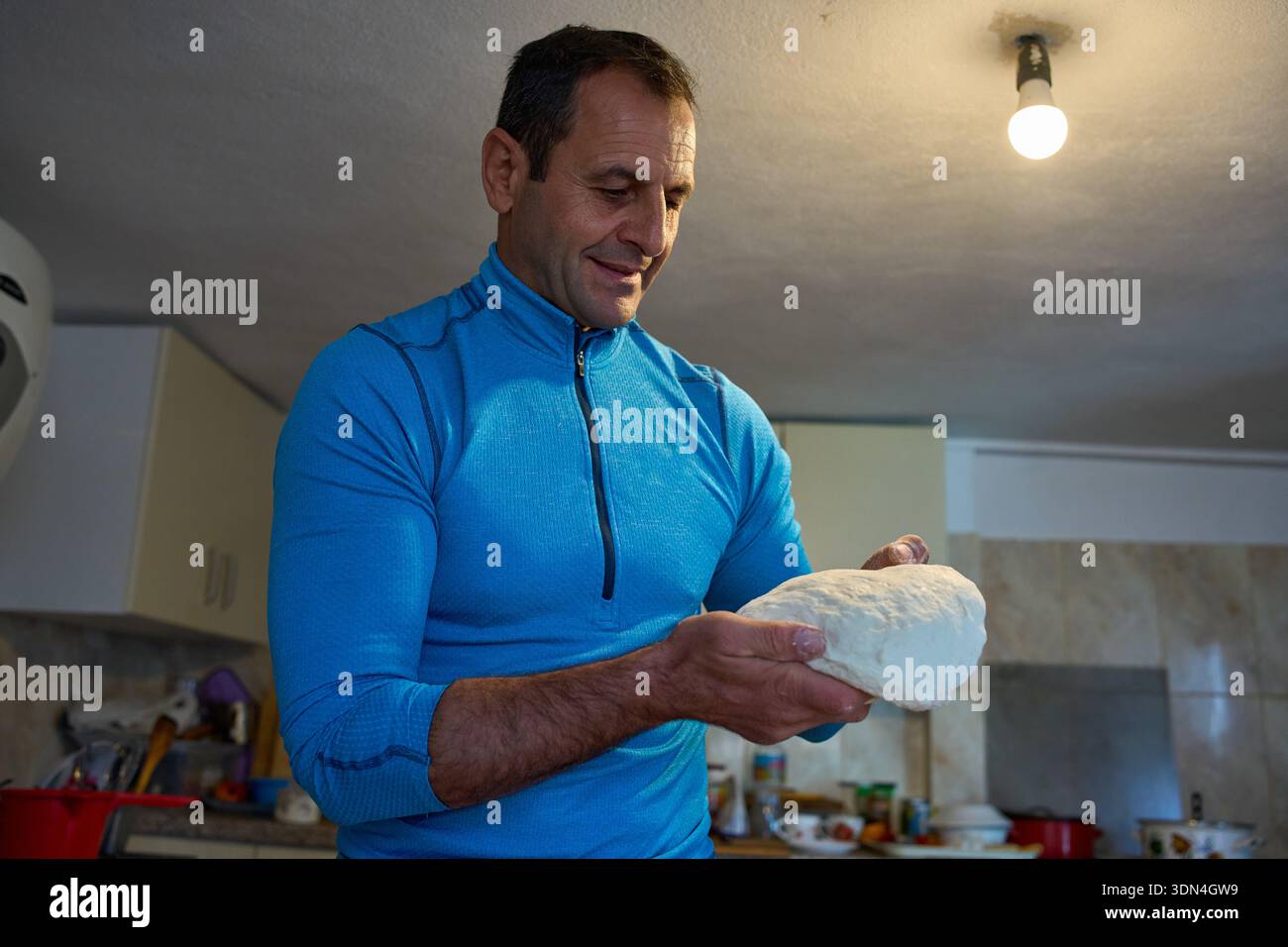 Homme d'âge moyen tenant et façonnant la pâte à pain dans les mains à la cuisine de la maison Banque D'Images