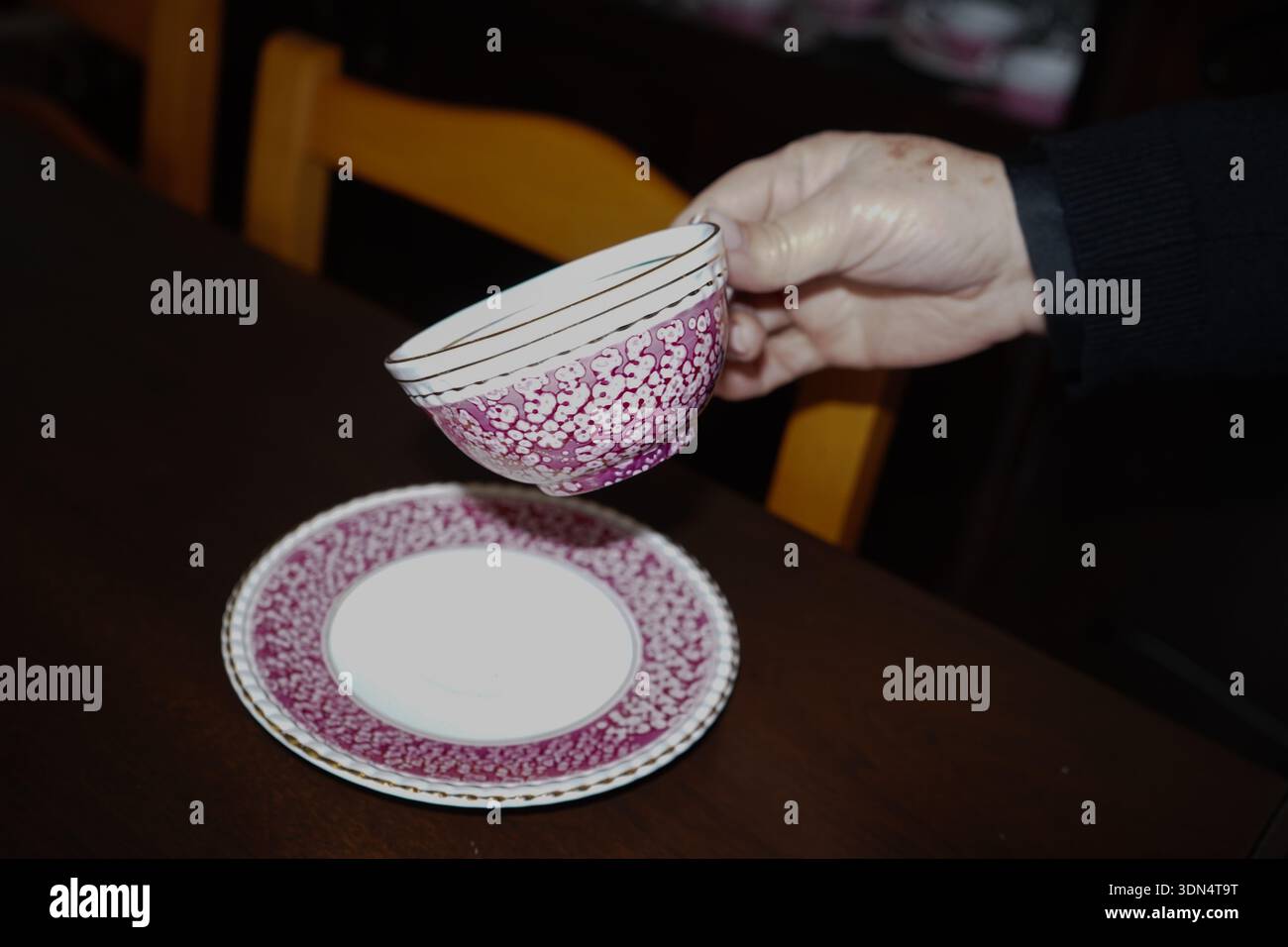Main tenant une tasse de thé en porcelaine vintage avec des motifs floraux roses et une soucoupe, l'heure du thé élégante dans une maison crétoise. Banque D'Images