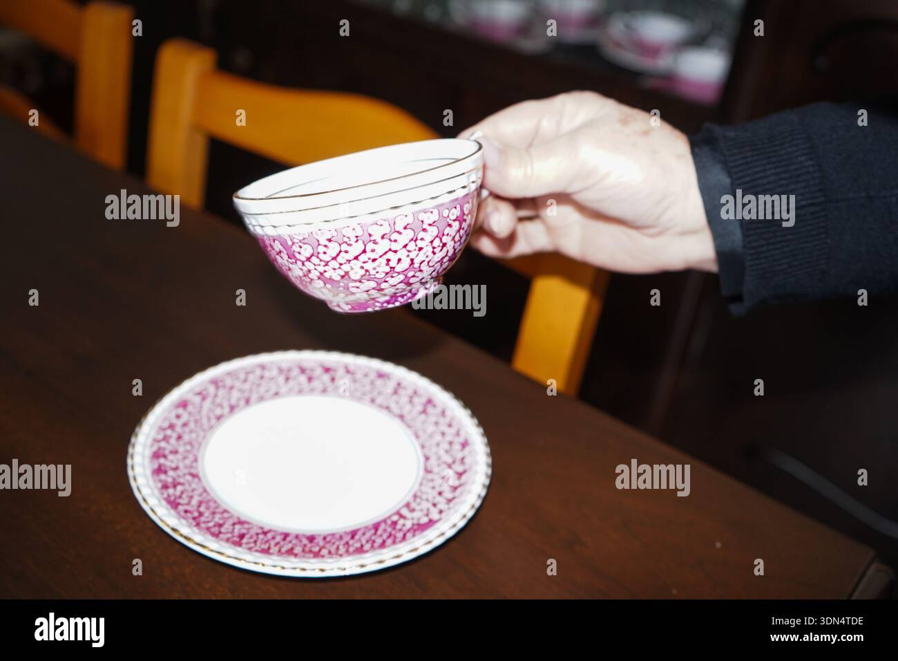 Main tenant une tasse de thé en porcelaine vintage avec des motifs floraux roses et une soucoupe, l'heure du thé élégante dans une maison crétoise. Banque D'Images