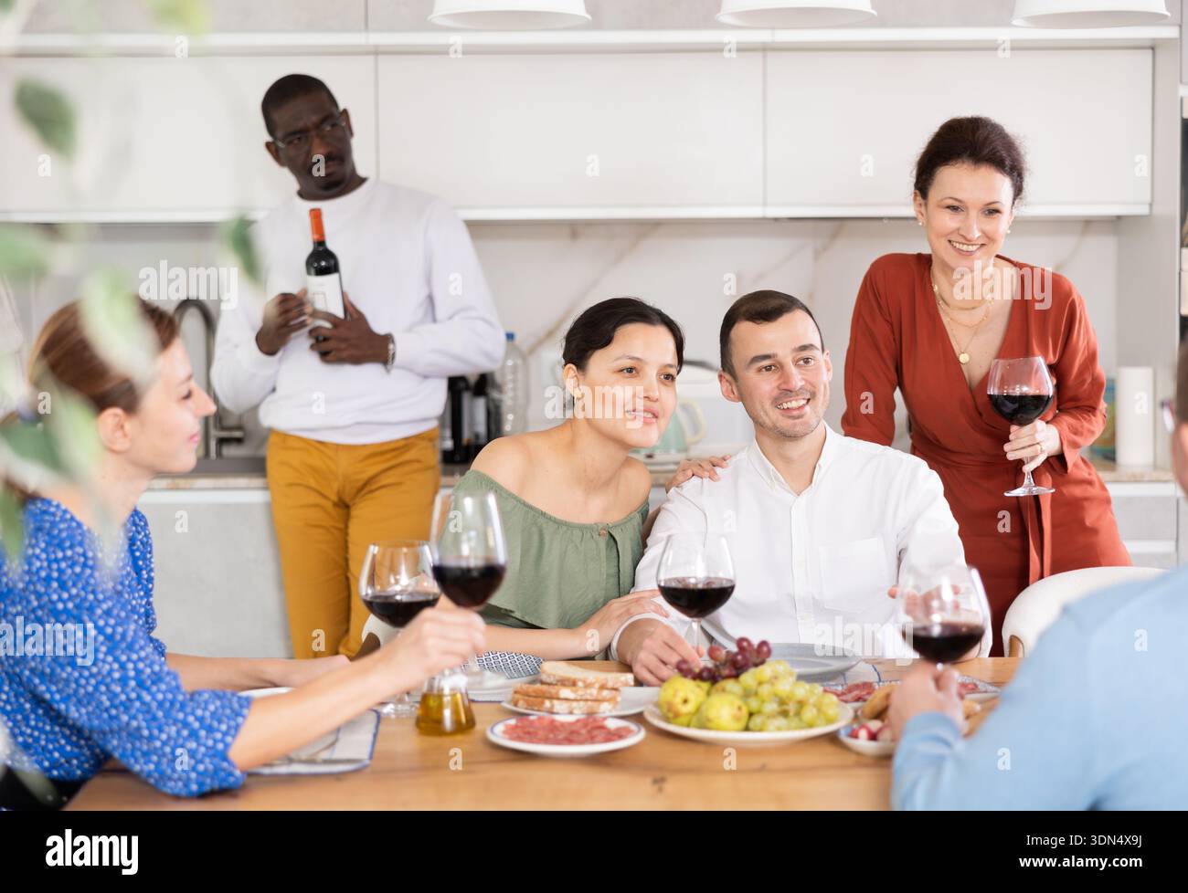 Les compagnons se sont rassemblés autour d’une table festive, participant à des discussions animées et dégustant les délices du vin rouge Banque D'Images