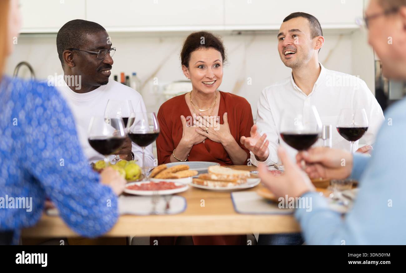 Les compagnons se sont rassemblés autour d’une table festive, participant à des discussions animées et dégustant les délices du vin rouge Banque D'Images