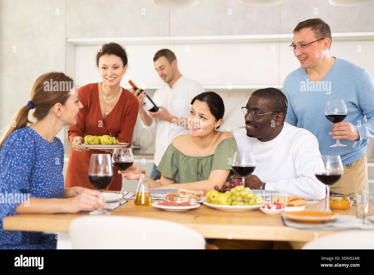 Les compagnons se sont rassemblés autour d’une table festive, participant à des discussions animées et dégustant les délices du vin rouge Banque D'Images