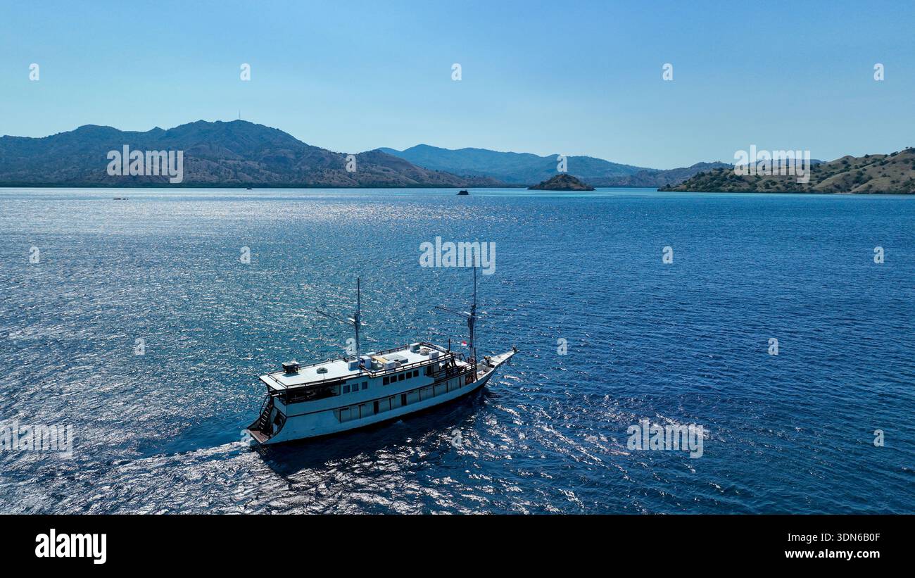 Un bateau en bois traditionnel indonésien phinisi flotte paisiblement sur des eaux calmes et bleu profond sous un ciel ensoleillé. Banque D'Images
